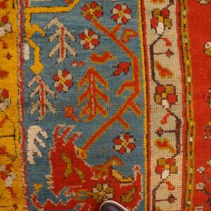 Close-up of a high pile rug in red, blue, and yellow on distressed wooden floorboards.