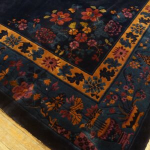 Deep navy high-pile rug with complex gold and teal floral borders displayed on worn wood flooring.