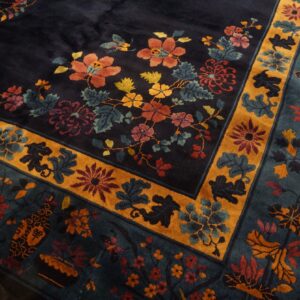 A dark blue rug with orange, red, and teal florals, featuring a prominent gold decorative border.