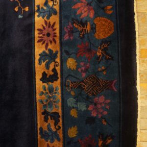 Navy and teal rug with intricate floral motifs in gold and rust rests on light yellow wood floor.