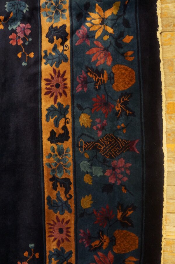 Navy and teal rug with intricate floral motifs in gold and rust rests on light yellow wood floor.