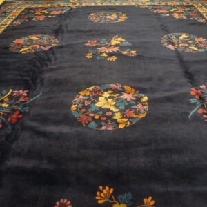 Dark blue rug with colorful floral medallions and sprays bordered in yellow and teal on wood flooring.