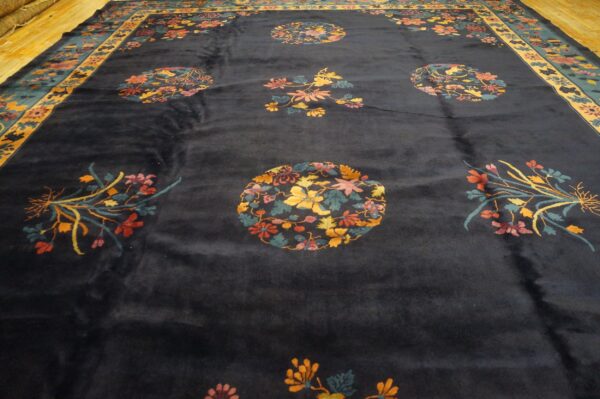 Dark blue rug with colorful floral medallions and sprays bordered in yellow and teal on wood flooring.