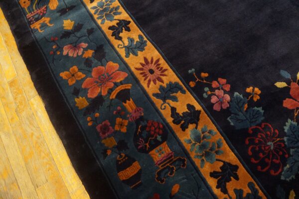 Ornate floral border in rust, teal, and gold on a dark navy rug lying on yellow wood planks.