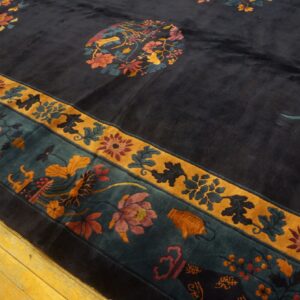 A plush navy rug with extensive multicolored floral patterns and gold borders rests on yellow hardwood flooring.