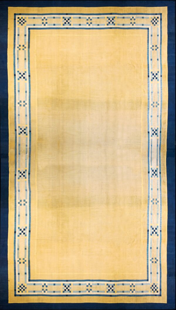 A low-pile pale yellow rug with dark and light blue geometric borders.