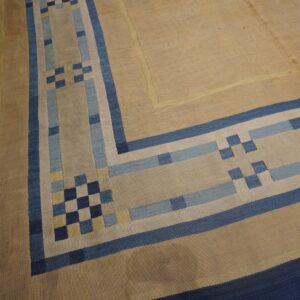 Geometric flatweave rug corner showing a tan field and stepped borders in navy, blue, and light blue.