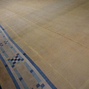 Low-pile tan rug featuring a wide linear border with blue and beige geometric blocks.