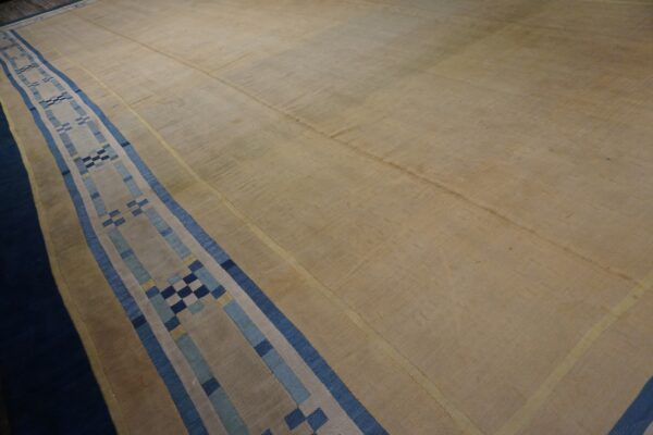 Low-pile tan rug featuring a wide linear border with blue and beige geometric blocks.