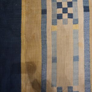 Striped flat weave rug in shades of navy, gold, and light blue with a central checkerboard design on wood floor.