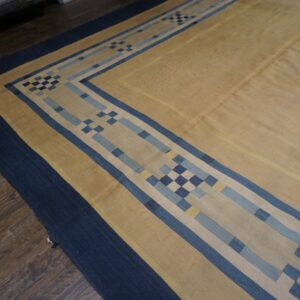Low-pile tan rug with a bold geometric blue border on dark wood flooring.