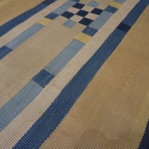 Geometric flatweave rug featuring wide tan and narrow blue, light blue, and cream stripes and block patterns.