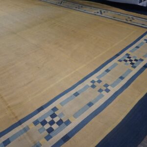 Tan flat woven rug bordered in navy and blue geometric patterns rests on dark wood floor.