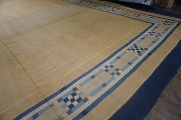 Tan flat woven rug bordered in navy and blue geometric patterns rests on dark wood floor.