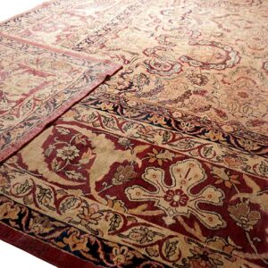 Traditional beige and deep red rug detail showing complex floral patterns and a folded corner.
