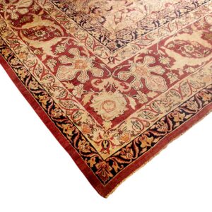 Low-pile rug corner displaying ornate traditional floral patterns in deep red, cream, and dark navy colors.