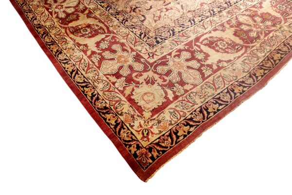 Low-pile rug corner displaying ornate traditional floral patterns in deep red, cream, and dark navy colors.