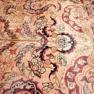 Low-pile traditional rug detail showing scrolling floral motifs in soft peach, deep red, and navy blue.