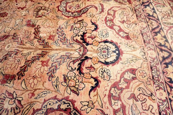 Low-pile traditional rug detail showing scrolling floral motifs in soft peach, deep red, and navy blue.