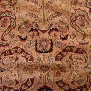Low-pile rug detail showing flowing paisley and floral patterns on a dusty tan field with burgundy accents.