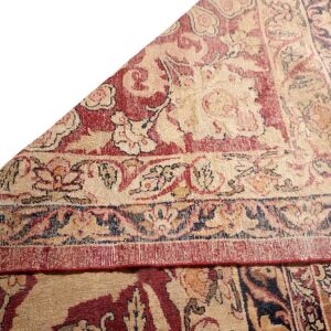 Low pile rug featuring worn red and beige floral motifs and intricate, layered border patterns.