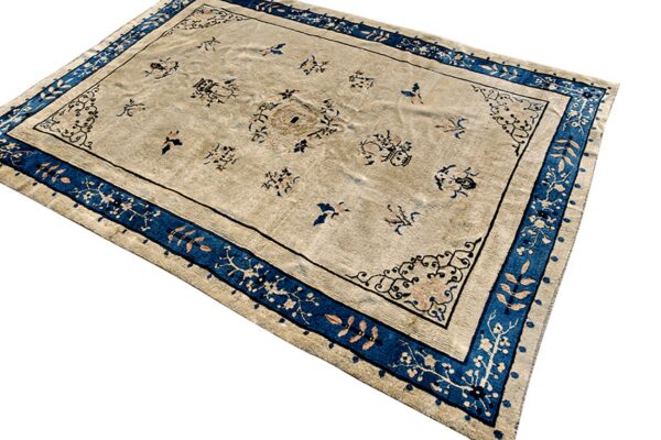 Low-pile tan rug featuring small blue and brown symbols, framed by a thick blue and beige floral border.