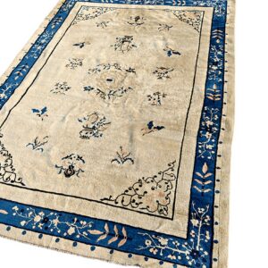 Light beige rug with scattered blue and pink motifs and a thick, stylized blue floral border.