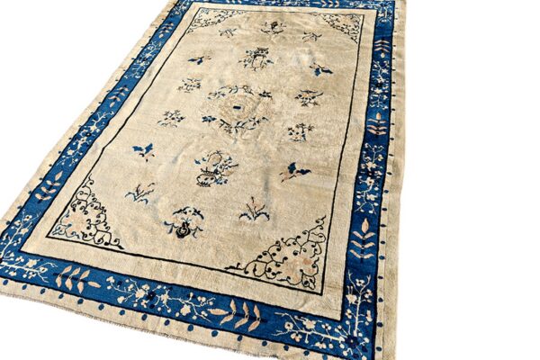 Light beige rug with scattered blue and pink motifs and a thick, stylized blue floral border.