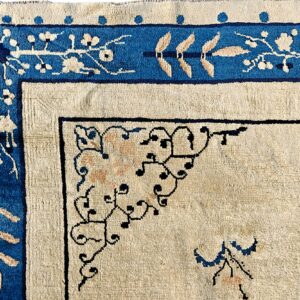 Cream rug corner featuring a thick blue border with ivory floral motifs and fine black scrollwork.