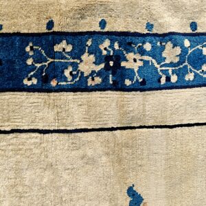 Textured beige rug detail features a wide royal blue border with light pink and cream botanical designs.