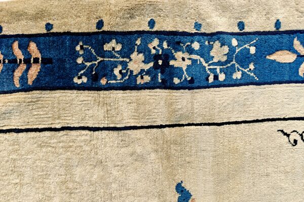 Textured beige rug detail features a wide royal blue border with light pink and cream botanical designs.