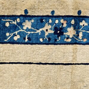 Cream rug detail showing a vibrant blue border with stylized floral patterns and thin dark blue accent lines.