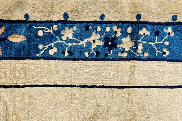 Cream rug detail showing a vibrant blue border with stylized floral patterns and thin dark blue accent lines.