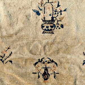 Textured cream pile rug with scattered traditional motifs in dark blue and pale pink accents.