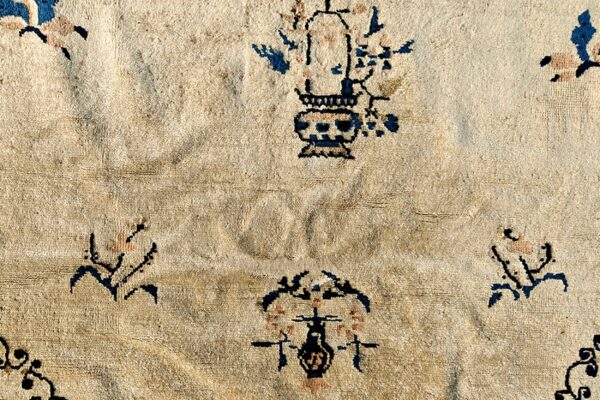 Textured cream pile rug with scattered traditional motifs in dark blue and pale pink accents.