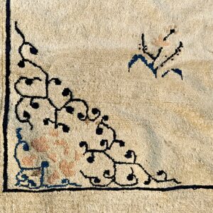 Cream rug detail showing a scrolling black vine corner pattern and a segment of a blue border.