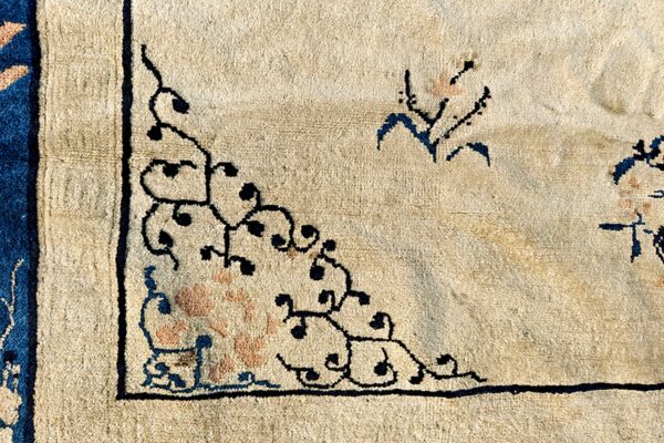 Cream rug detail showing a scrolling black vine corner pattern and a segment of a blue border.