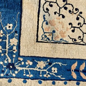 Detailed view of a rug corner featuring blue, cream, and peach floral borders and scrolling dark patterns.