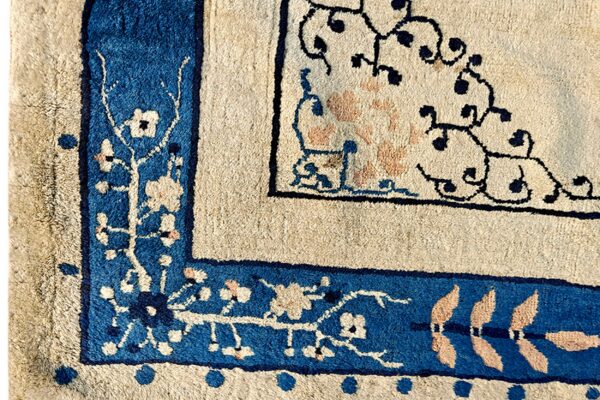 Detailed view of a rug corner featuring blue, cream, and peach floral borders and scrolling dark patterns.
