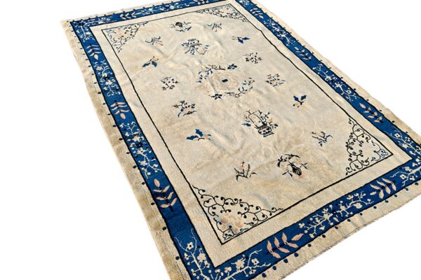 A cream rug with scattered blue floral motifs and a wide blue border with light pink leaves.