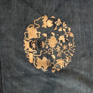 Deep teal rug detail featuring a circular golden beige medallion of stylized flowers and vines.