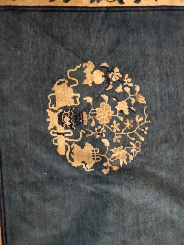 Deep teal rug detail featuring a circular golden beige medallion of stylized flowers and vines.