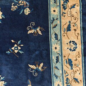 Navy blue rug with scattered beige flowers and butterflies next to a detailed tan and teal floral border.