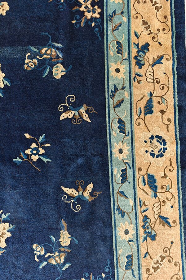 Navy blue rug with scattered beige flowers and butterflies next to a detailed tan and teal floral border.