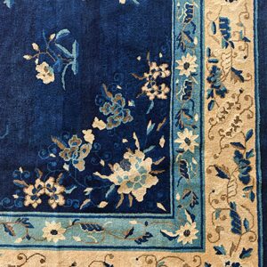 A deep blue rug with cream, teal, and tan floral designs along the corner border.