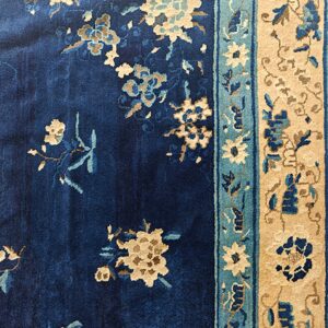 Navy blue plush rug featuring scattered beige and blue florals and layered tan and teal borders.