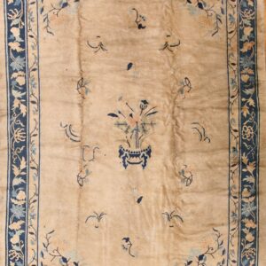 Tan low-pile rug with navy borders and sparse blue and pale pink floral designs, including a central vase motif.