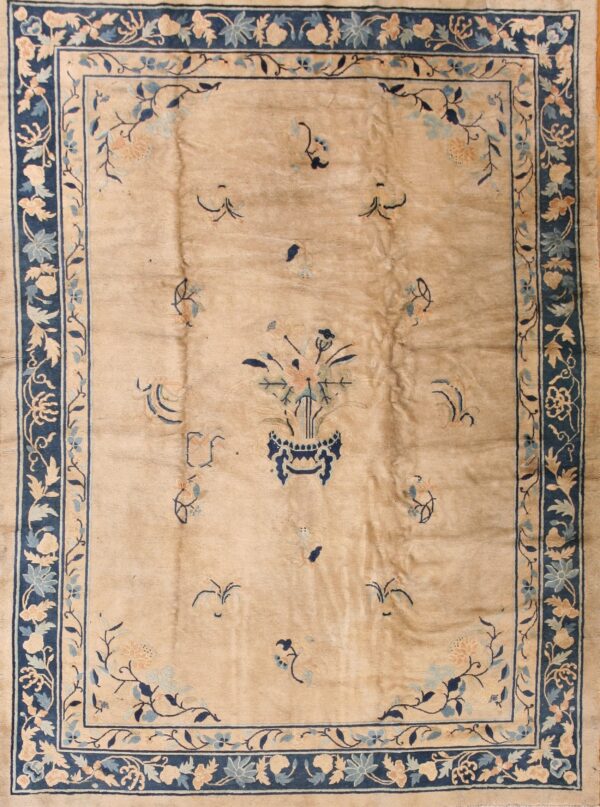 Tan low-pile rug with navy borders and sparse blue and pale pink floral designs, including a central vase motif.