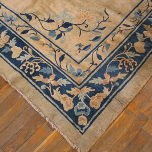 Close-up of a tan rug with an ornate blue floral border resting on worn wood planks.