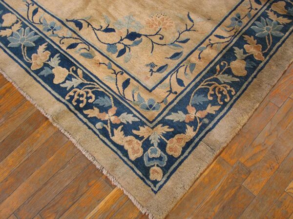 Close-up of a tan rug with an ornate blue floral border resting on worn wood planks.